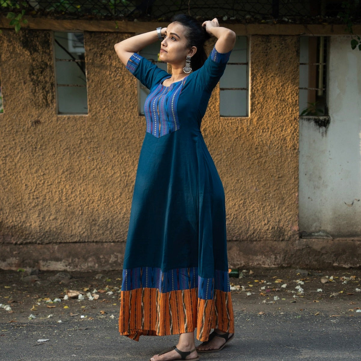 A woman modeling a long teal blue dress with blue and orange ikat details.